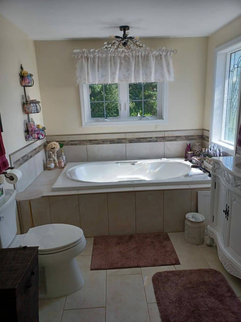 A bright bathroom with a white bathtub, toilet, and vanity, featuring a decorative clear leaded glass privacy window on the right side.