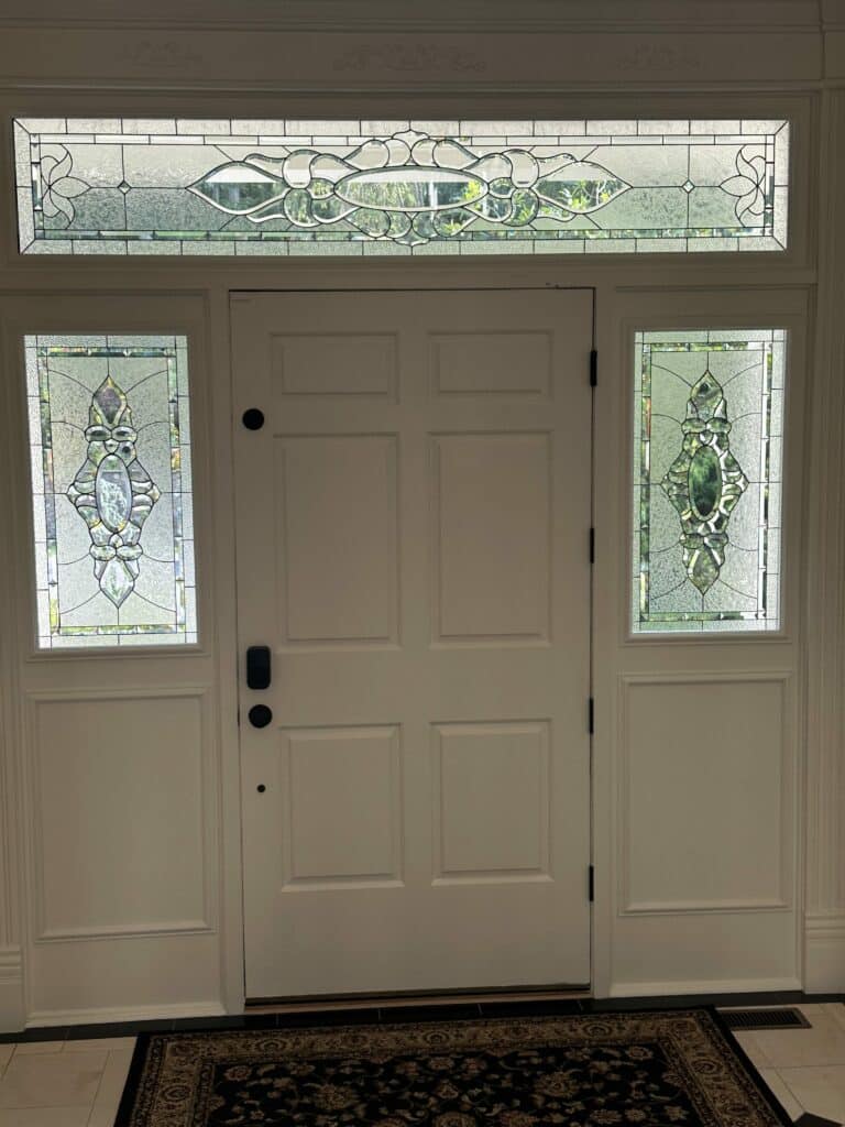 A traditional white front door with two vertical clear beveled stained glass sidelights and a horizontal clear textured glass transom. The panels feature an elegant design of stylized leaves and floral motifs with clear bevels, creating privacy.