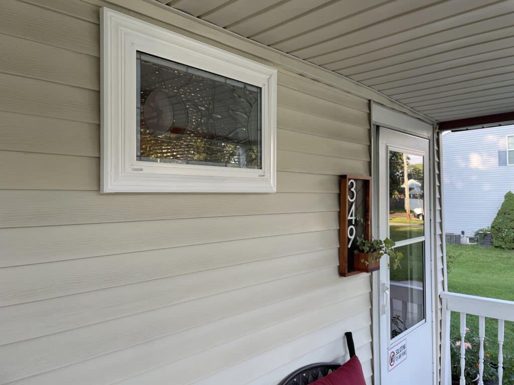 A rectangular white-framed window featuring a clear leaded glass insert with a prominent circular design on the left and abstract textured glass patterns throughout.