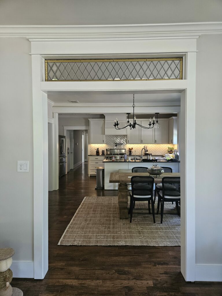 A rectangular stained glass transom panel featuring clear diamond-shaped beveled glass and a gold-toned border, installed above a white-trimmed interior doorway leading to a kitchen.