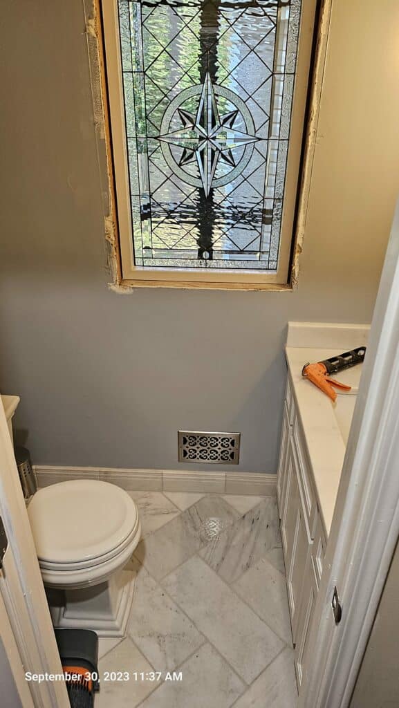 A rectangular, leaded stained glass window featuring a central star or compass rose medallion, surrounded by clear geometric textured and beveled glass.