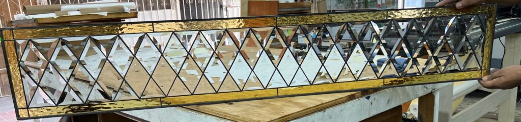 A rectangular stained glass panel featuring a central design of clear beveled diamonds and triangles, bordered by textured amber glass and dark lead lines.