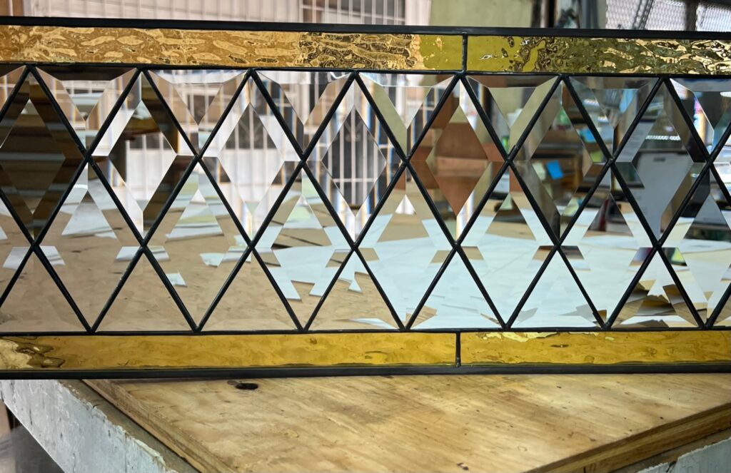 A rectangular stained glass panel featuring a central section of clear beveled diamond-shaped glass, bordered above and below by textured golden-yellow glass.