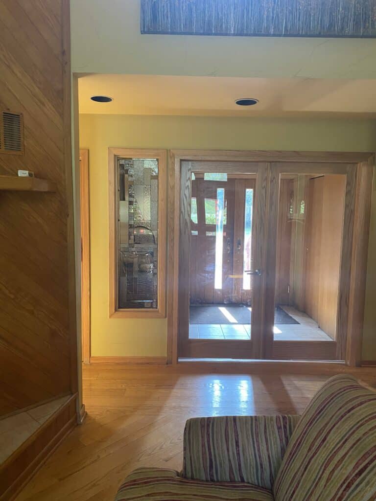 A tall rectangular stained glass sidelight panel next to French doors, featuring an abstract geometric pattern created with various clear, textured, and beveled glass pieces, all set in a natural wood frame.