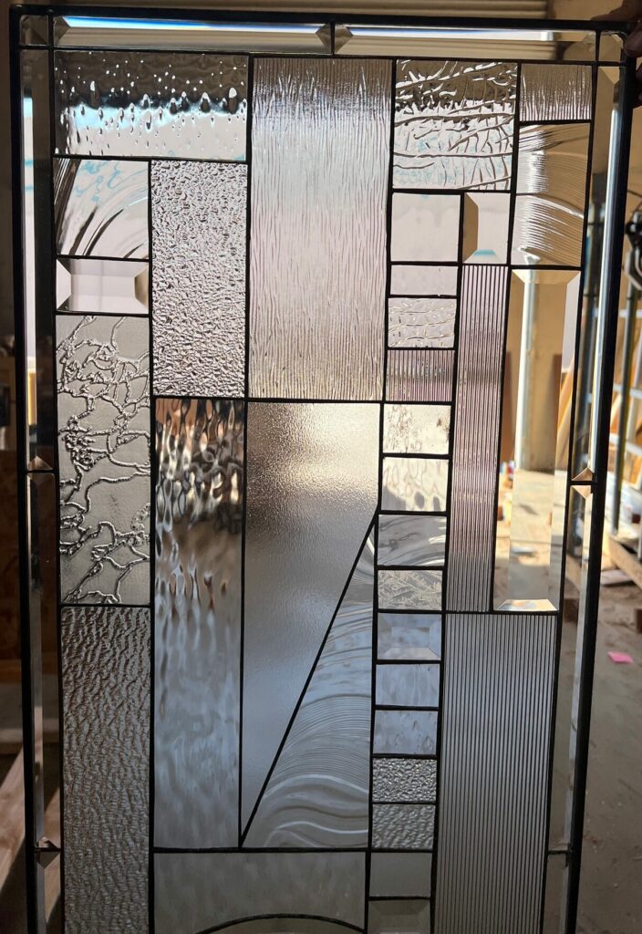 A rectangular leaded stained glass panel featuring an abstract geometric design crafted from a variety of clear textured and beveled glass types.