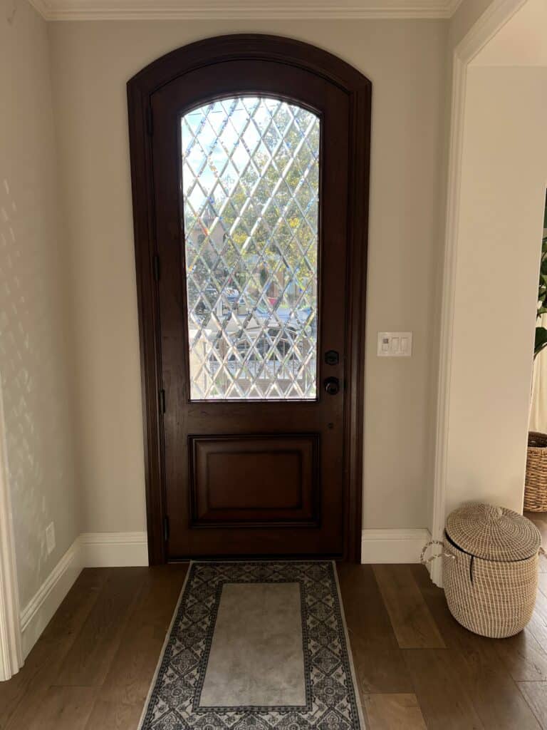 A dark wooden arched entry door featuring a large clear beveled diamond-patterned stained glass panel, seen from an interior entryway.