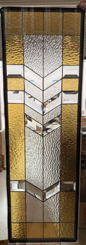 A vertical rectangular leaded stained glass panel featuring a prominent central chevron pattern of clear beveled glass, flanked by textured amber and clear glass rectangles.