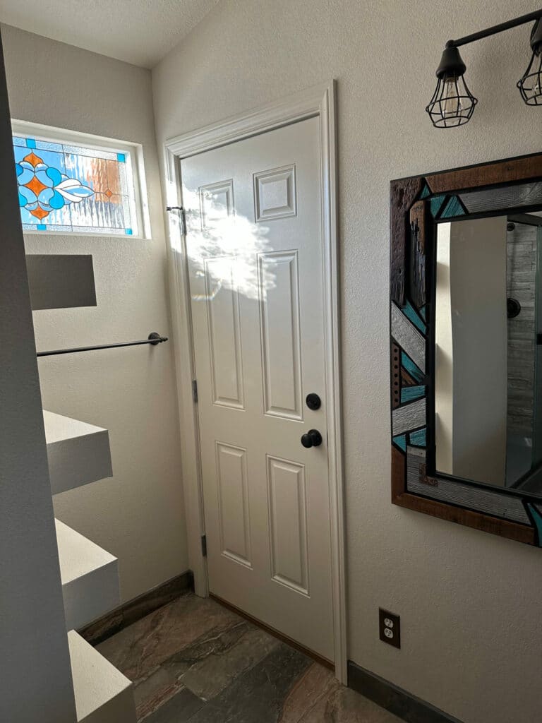 A rectangular stained glass window featuring a central stylized floral or leaf-like design in blue, light blue, and orange glass, surrounded by clear textured glass.