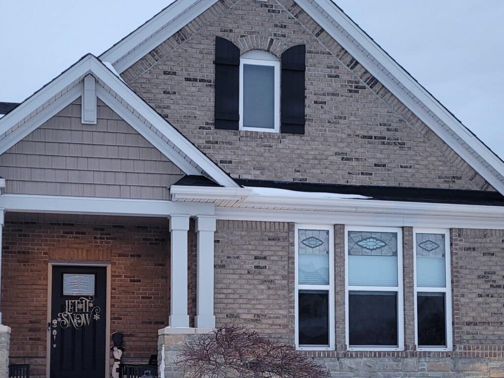 Three rectangular house windows, each featuring an upper transom panel with a clear textured stained glass medallion design in muted colors, set against a brick wall.