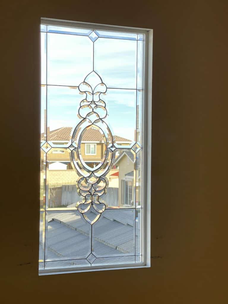 A rectangular clear beveled and leaded glass window with an ornate central oval and scroll design, set in a white frame.