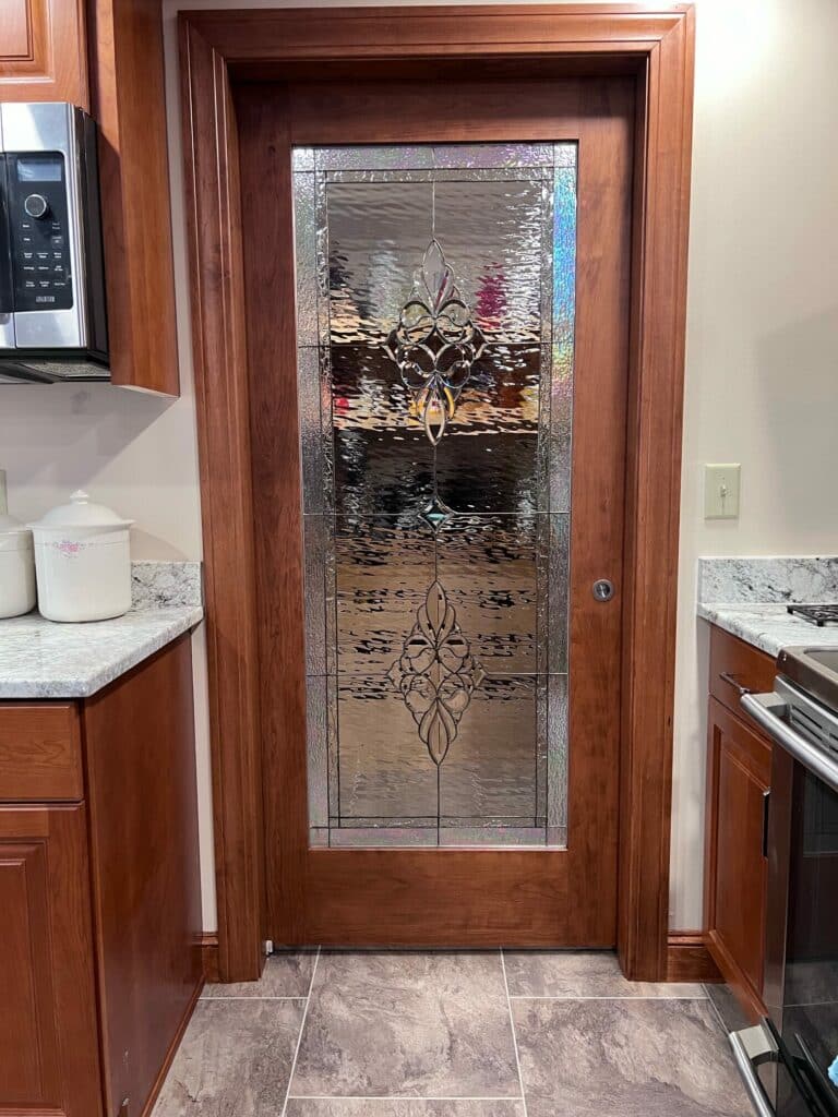 A full-light cherry wood door with a clear textured stained glass panel featuring two ornate beveled fleur-de-lis motifs.