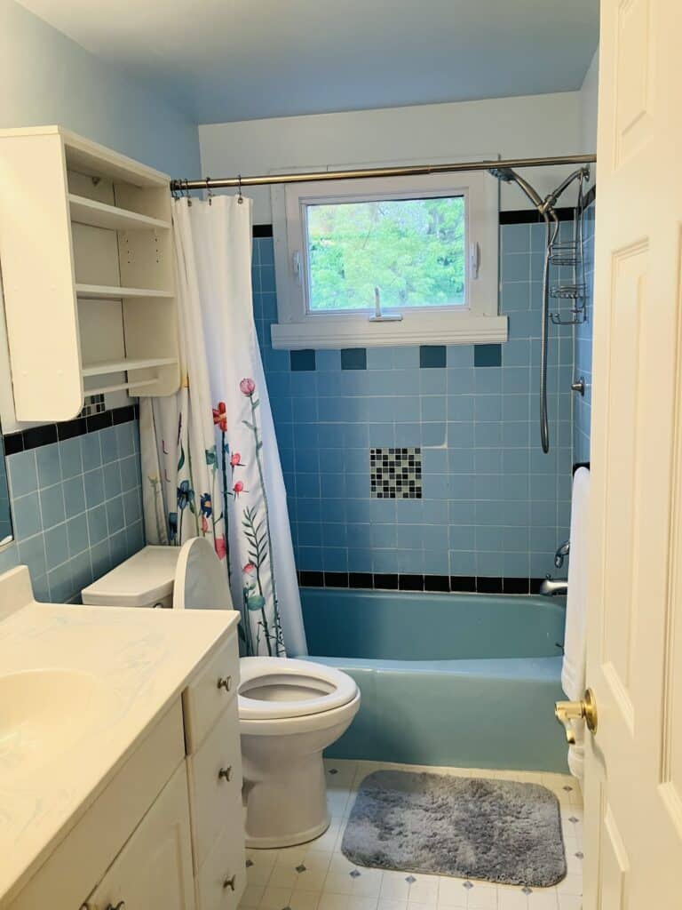 A rectangular leaded stained glass panel featuring shades of aqua and sky blue, with clear textured glass and a subtle ripple design, set into a bathroom window.