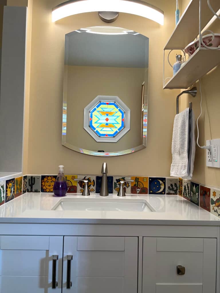 An octagonal stained glass panel with a vibrant geometric pattern in blue, yellow, orange, and red, featuring stepped and diamond motifs inspired by Southwestern design.