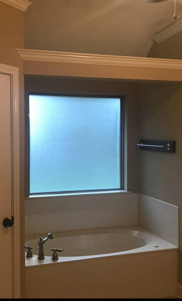 A rectangular stained glass window, featuring an abstract geometric design with clear textured and bevelled glass, providing privacy in a bathroom setting above a built-in tub.