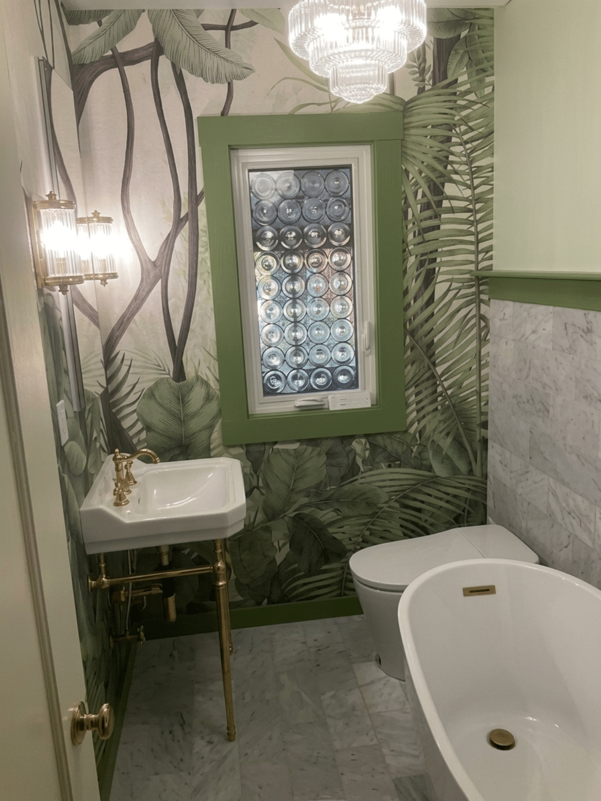 A rectangular leaded glass window featuring numerous clear glass roundels, installed in a green-trimmed window frame in a bathroom with tropical leaf wallpaper.