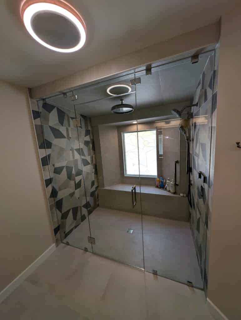 A clear, patterned glass window with a minimalist geometric grid design, set within a contemporary tiled shower enclosure.