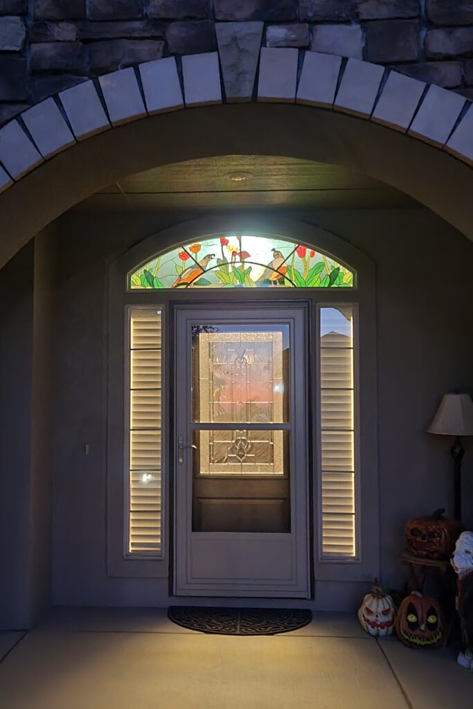 An arched stained glass transom window featuring two quails among red and orange tulips and green foliage, above a white front door with decorative glass panels.