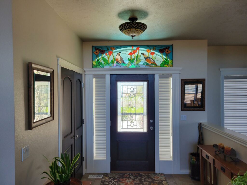 A rectangular stained glass transom depicting two quail-like birds among vibrant red poppies and green foliage, set against a light blue background, positioned above an entryway door with clear beveled glass.