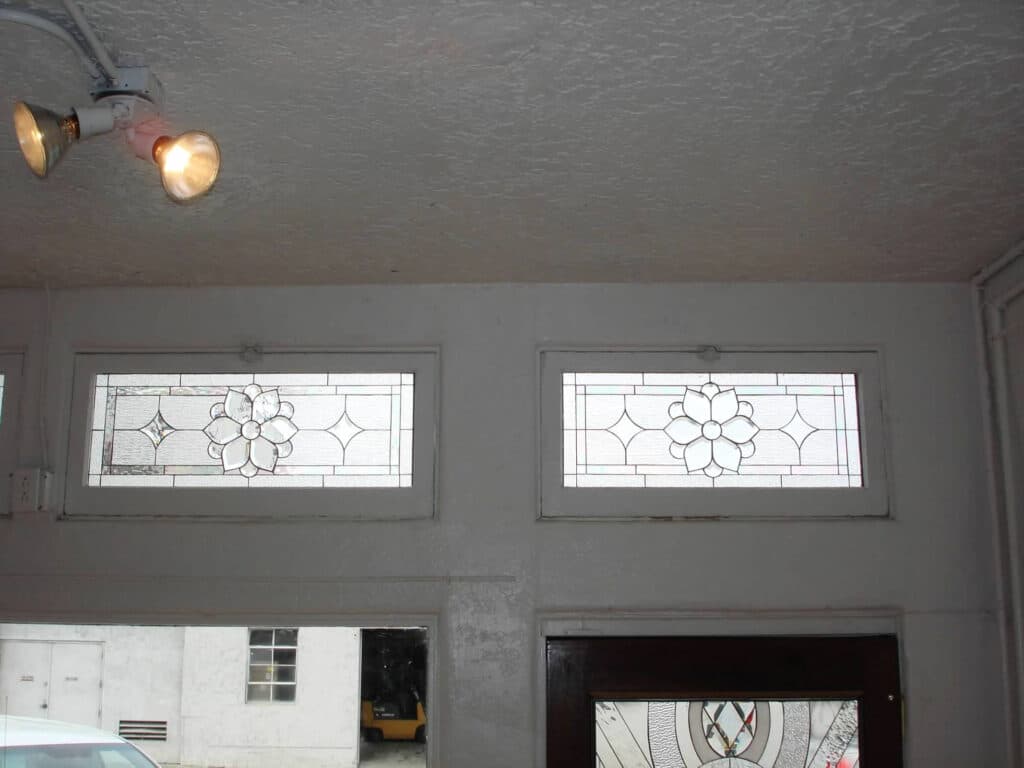 A pair of rectangular clear stained glass transom windows, each featuring a central beveled floral medallion surrounded by clear textured geometric panels.