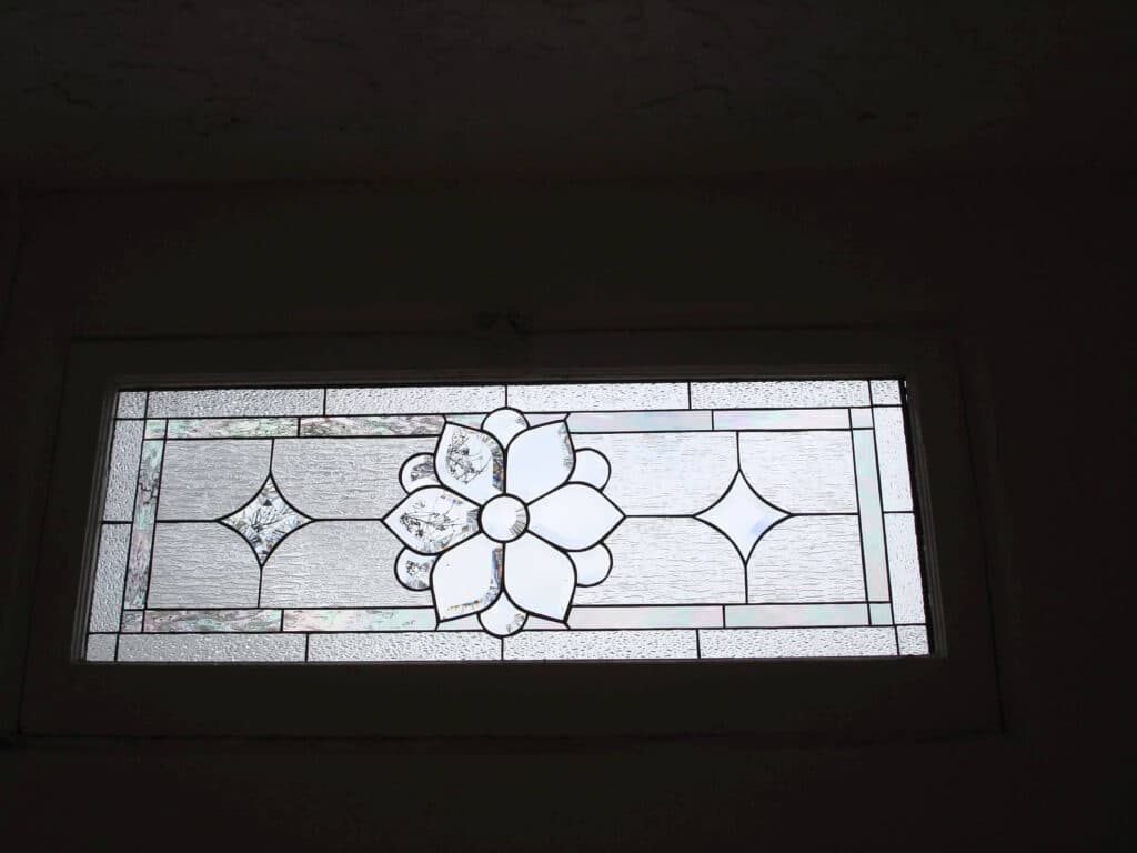 A rectangular leaded stained glass window featuring a central clear floral medallion with textured clear glass and diamond accents.