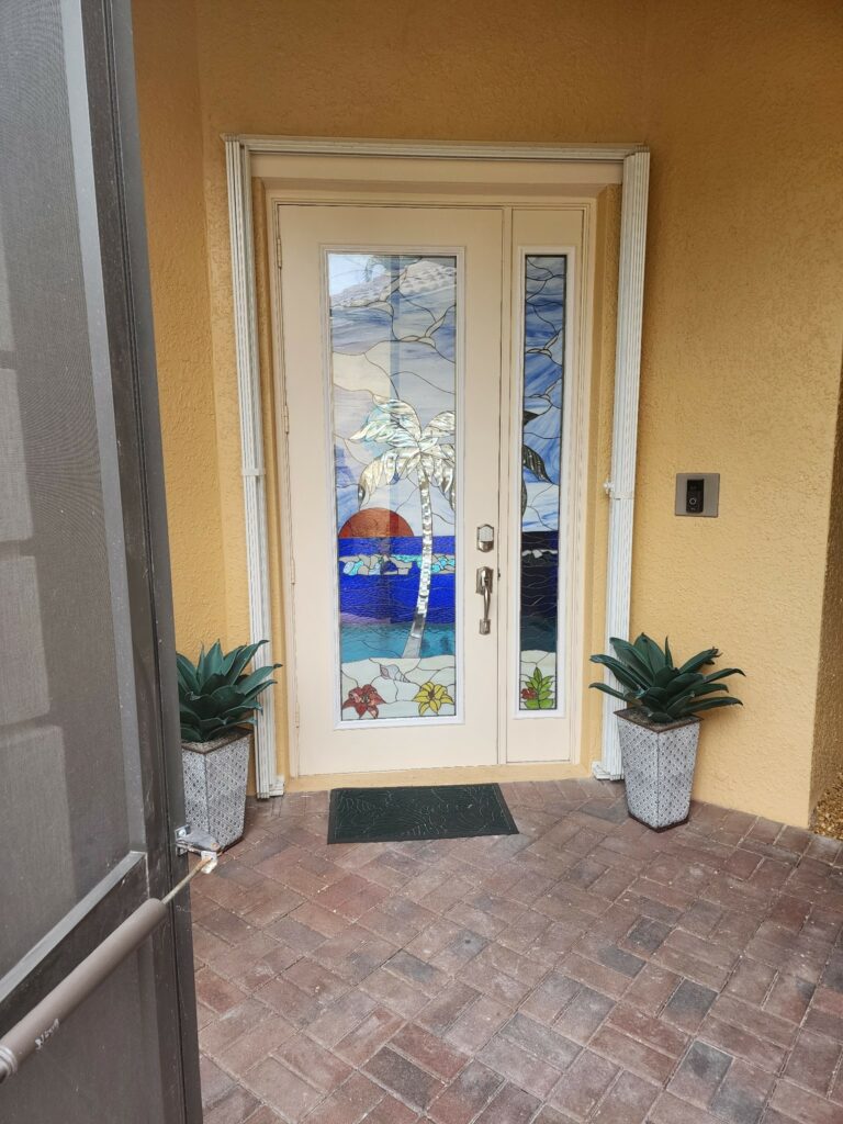 Leaded stained glass double entry door featuring a tropical scene with a palm tree, red sunset, and blue ocean, flanked by two narrow matching side panels.