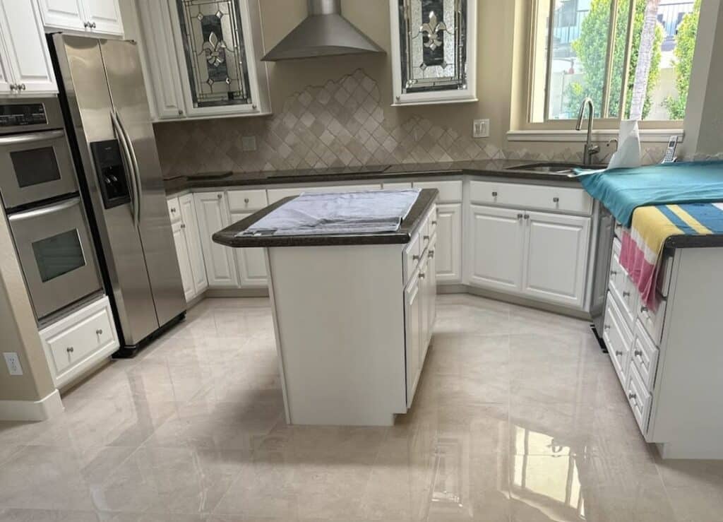 Two rectangular stained glass panels, each with a clear textured glass fleur-de-lis design and dark lead lines, set into white kitchen cabinet doors.
