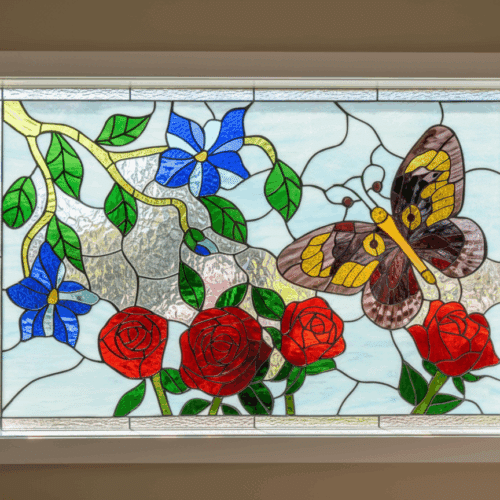 A rectangular, leaded stained glass window panel featuring a colorful butterfly, red roses, and blue flowers on a light blue background with clear textured glass.