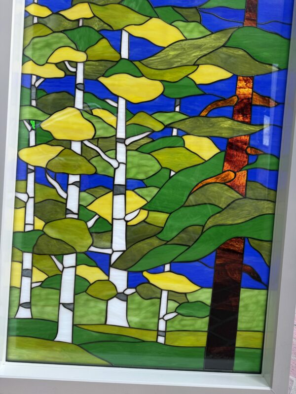 A rectangular stained glass panel depicting an abstract forest scene with white birch trees, green and yellow leaves, a dark brown tree, and a bright blue sky, set in a white frame.