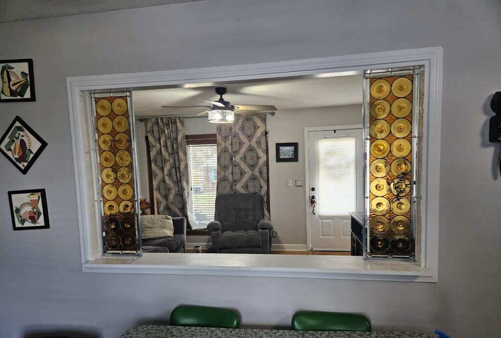 Two rectangular stained glass panels, each featuring columns of circular, amber-colored glass pieces set within a clear beveled frame, installed in a room divider opening.