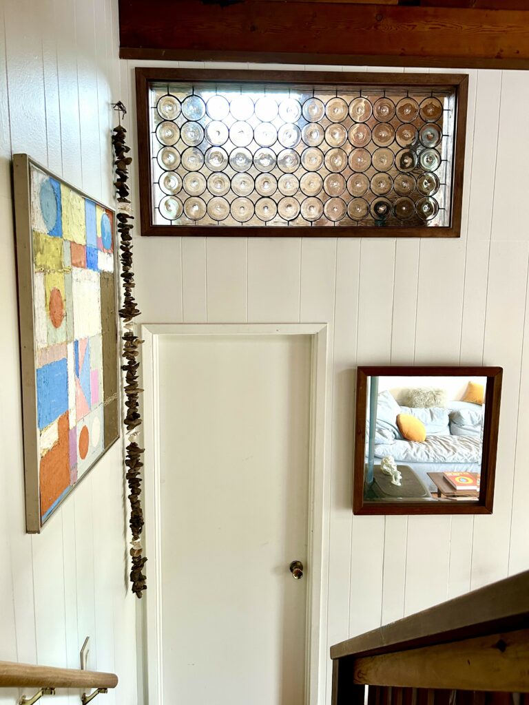 A rectangular clear stained glass transom window, featuring numerous circular pressed glass rondels set in a dark leaded matrix within a warm brown wooden frame, positioned above a white interior door.