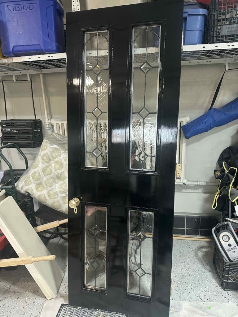 A glossy black entry door featuring four clear leaded glass panels. Each panel includes textured swirling glass, clear diamond bevels, and arched top bevels, all set in metal caming. A brass doorknob is on the right side.