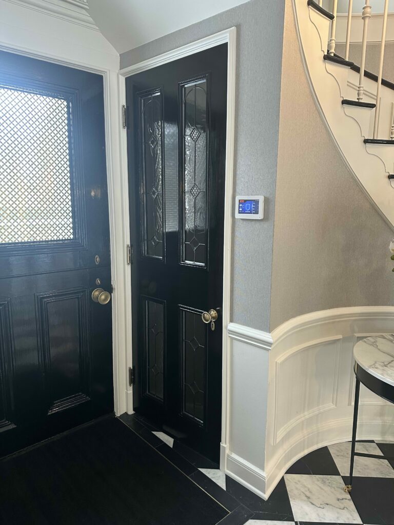 A sleek black front door featuring clear bevelled and textured leaded glass panels in a geometric design, alongside a second door with privacy patterned glass, in a modern entryway with a checkered floor and white staircase.
