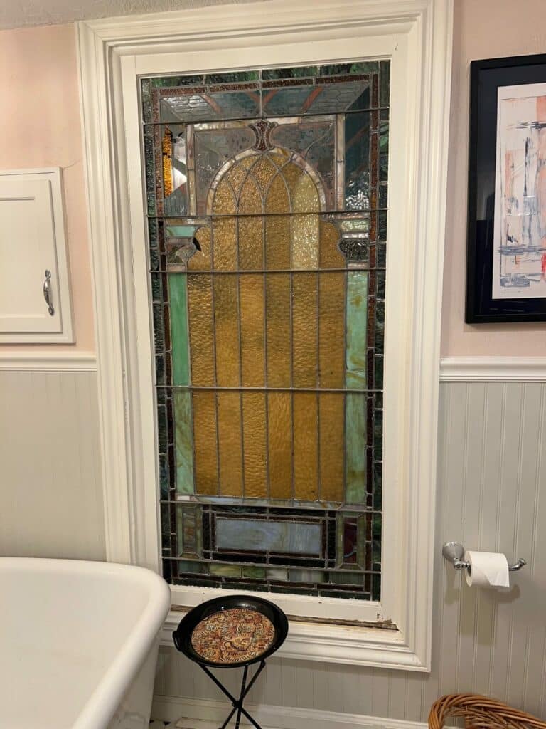 Rectangular leaded stained glass window with a central textured amber arched design, framed by geometric green and brown glass.