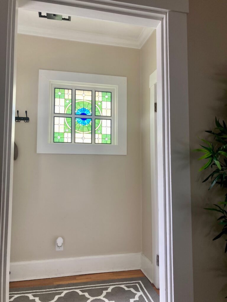 A rectangular stained glass window with a central blue eye-like medallion, surrounded by geometric green and clear glass.