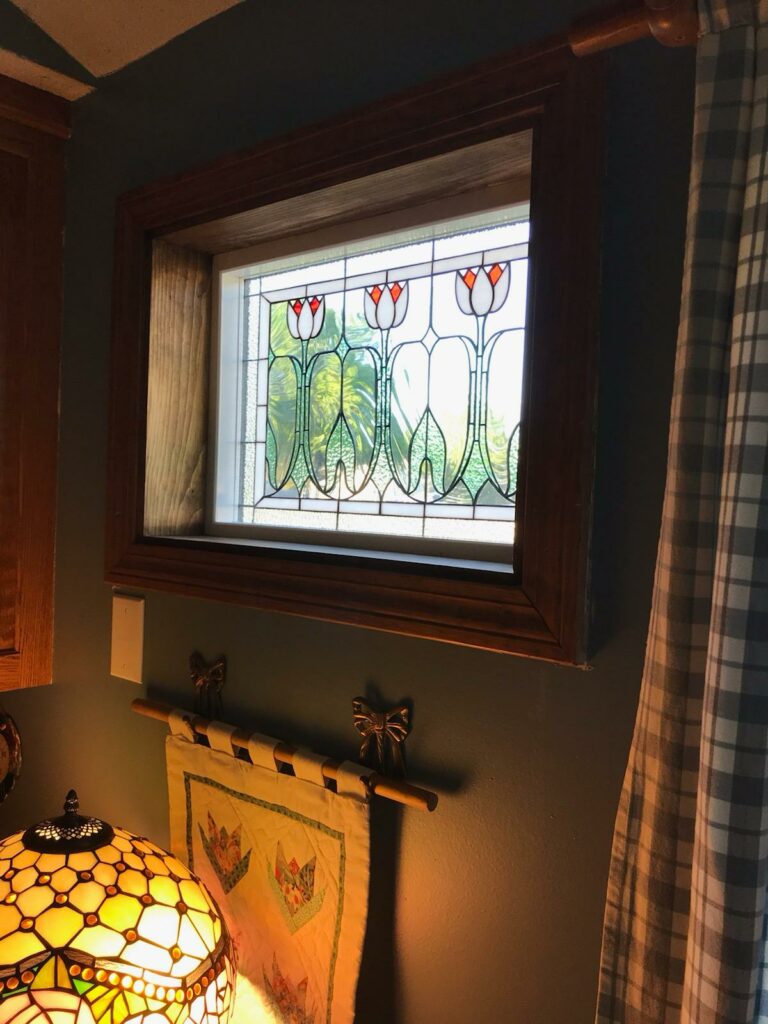 A rectangular stained glass panel in an Arts & Crafts style, featuring stylized white tulips with red-orange centers and green stems, set in a clear textured background within a deep wooden window frame.