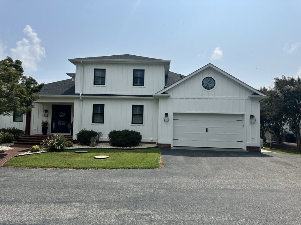 A round, clear stained glass window with a blue nautical compass rose and anchor design, set within the white gable of a modern house above the garage.