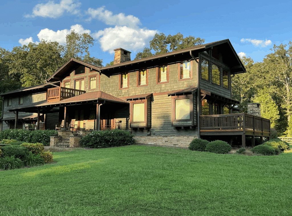 A large Craftsman-style house with green shingle siding, featuring multiple rectangular stained glass transom windows with amber and clear geometric patterns on the upper level.