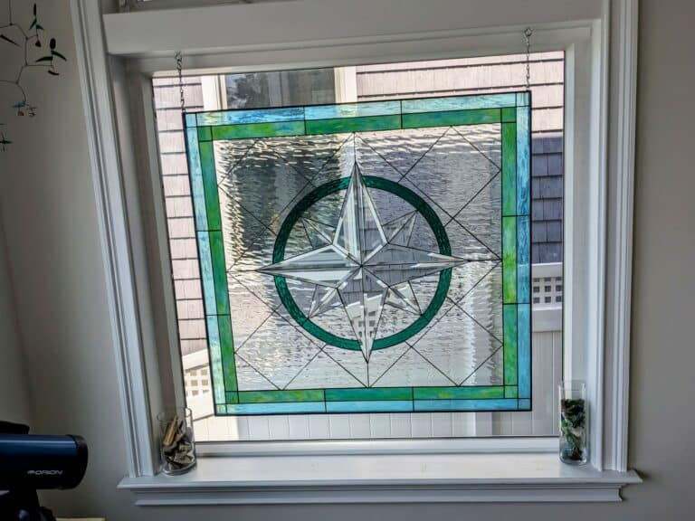 A square leaded stained glass panel with a central clear bevelled compass rose design, bordered by green and light blue glass.