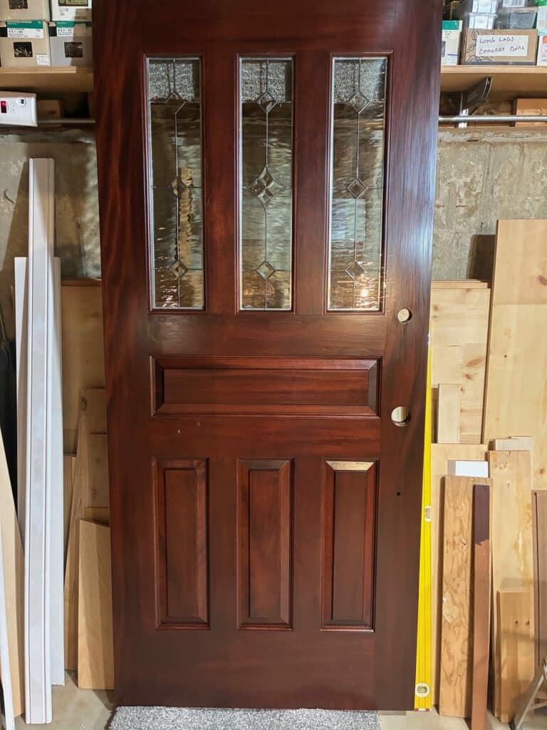 A dark wooden door featuring three vertically aligned rectangular clear textured stained glass inserts with geometric beveled accents and pebbled privacy glass at the top.