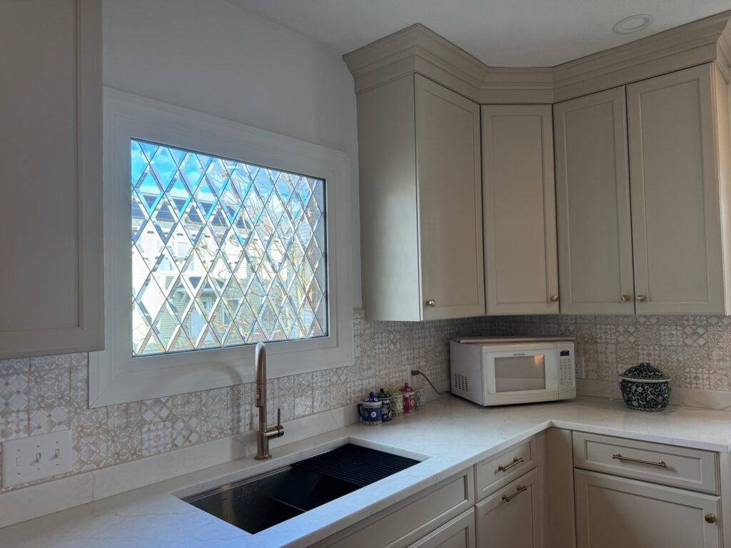 A rectangular, leaded window featuring clear beveled glass arranged in a diamond pattern, installed in a kitchen above a sink.