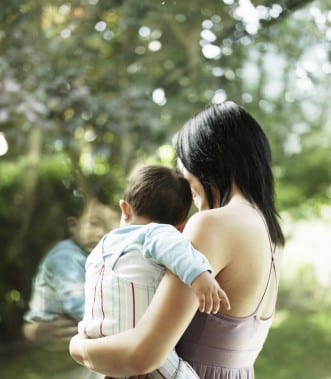 A rectangular stained glass panel depicting a woman holding a baby, with a faint, ghost-like reflection of another child rendered in translucent glass.