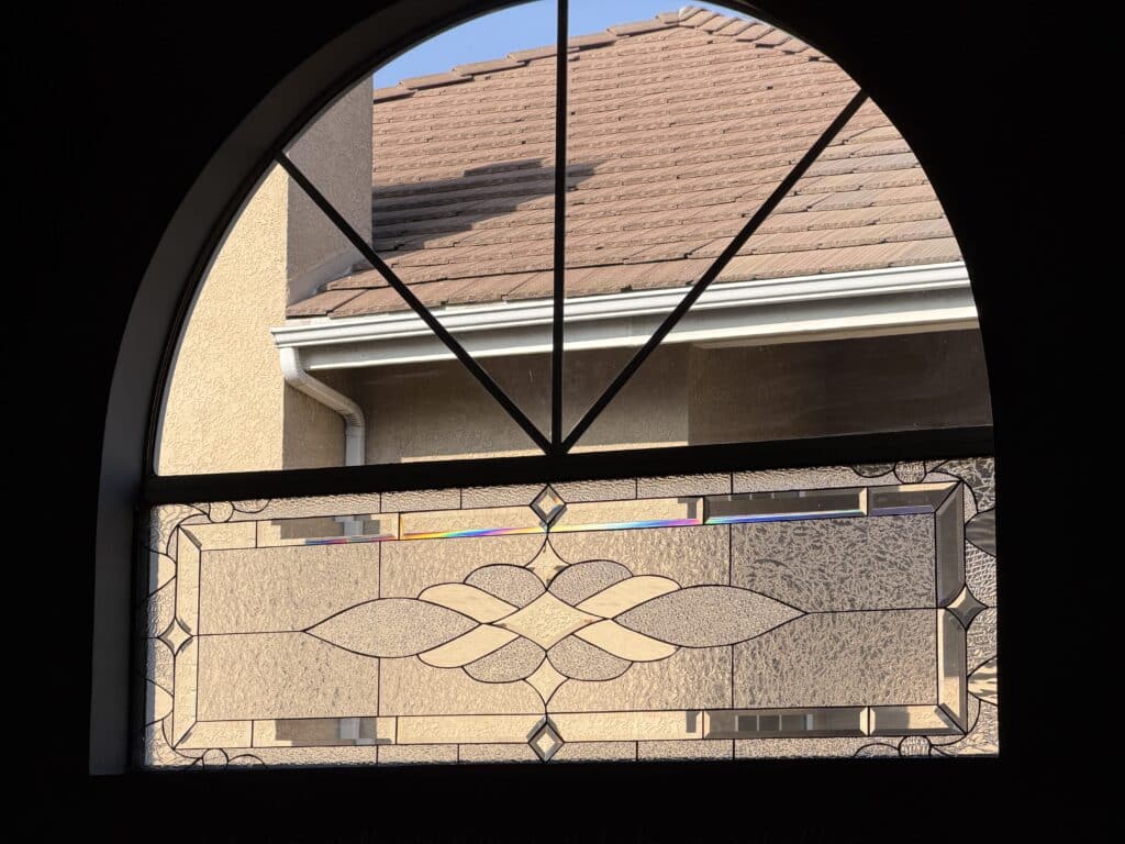 An arched window featuring a rectangular clear stained glass panel with a geometric design, textured glass, and prismatic bevels.