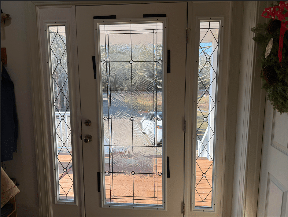 A white double entry door with two rectangular sidelights, all featuring clear leaded glass. The main door panels have a wavy textured center framed by geometric rectangles and circles, while the sidelights display a diamond pattern with small circles.