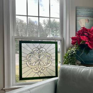 Rectangular Leaded Clear Beveled Scrollwork Panel A rectangular leaded stained glass panel featuring a clear beveled scrollwork medallion with radiating clear textured glass, framed by a dark green border. The panel hangs in a double-hung window, offering privacy while allowing light.