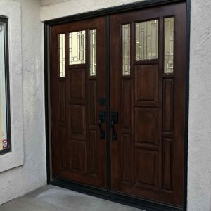 Geometric Leaded Glass Double Entry Doors Dark brown double entry doors with black hardware, featuring clear geometric leaded glass panels in the upper sections, set in a light stucco wall.