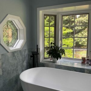 Octagonal Clear Bevel and Textured Stained Glass Window An octagonal stained glass window featuring a clear beveled and textured medallion design, set in a white frame on a light blue wall above a bathtub.